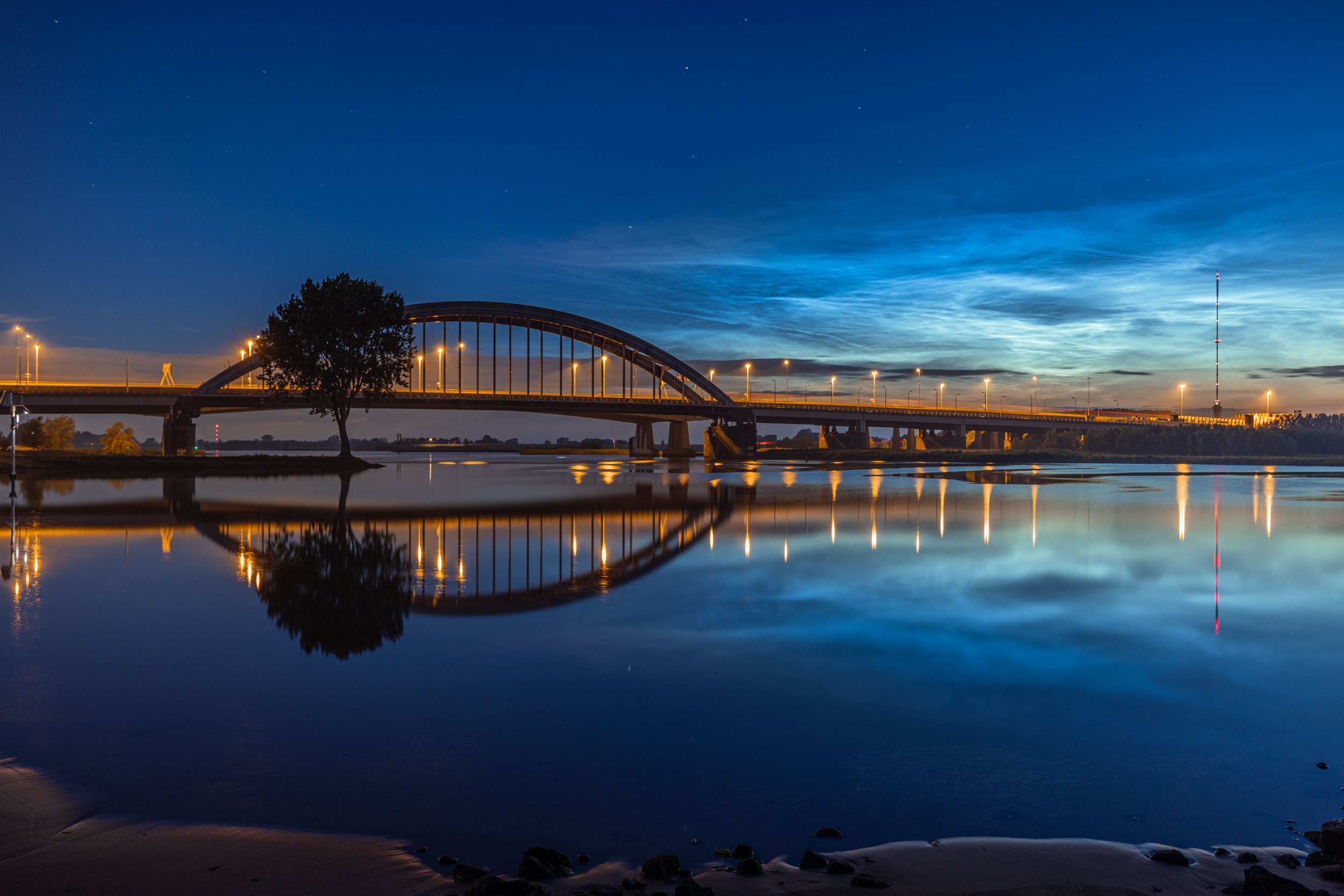 Lichtende nachtwolken boven een boogbrug, weerspiegeld in het stille water