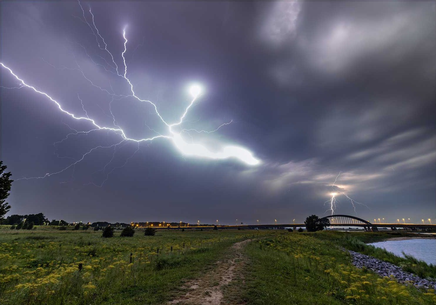 Een bliksemschicht boven het weiland, met de Lekbrug in de verte